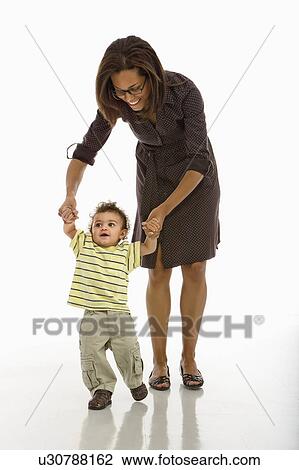 Stock Image - Mother holding arms of toddler son learning to walk. Fotosearch