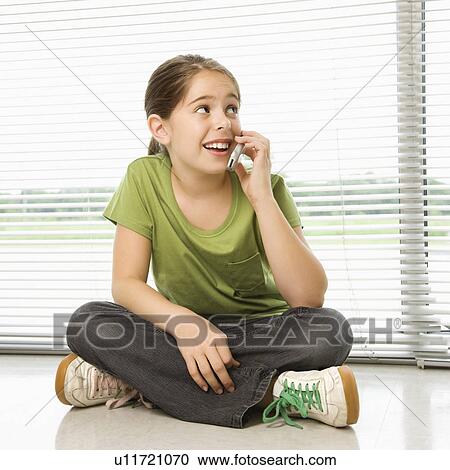 Stock Image - Preteen girl sitting on floor talking on cell phone. Fotosearch