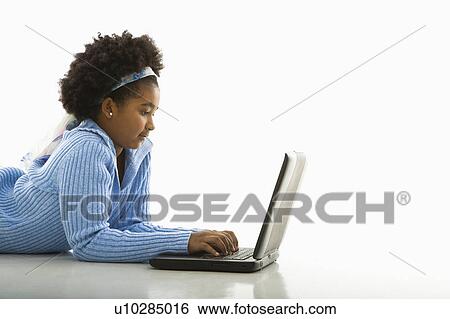 Stock Photograph - Side view of African American girl lying on floor using laptop.. Fotosearch
