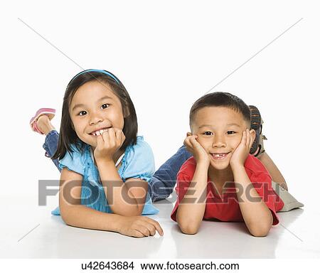 Picture - Young brother and sister lying on floor with head on hands. Fotosearch