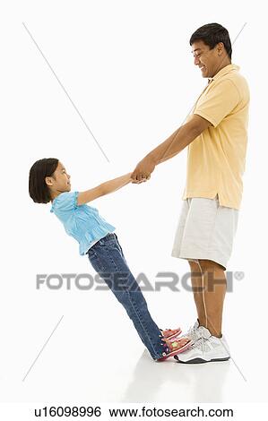 Stock Photograph - Asian daughter standing on father's feet holding his hands and leaning back.. Fotosearch