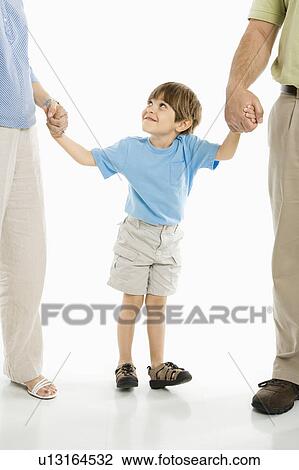 Stock Image - Boy holding hands with parents standing against white background.. Fotosearch
