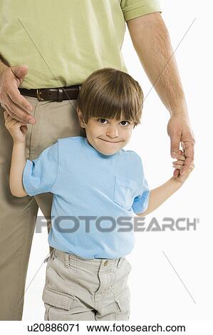 Stock Image - Boy holding onto father's hands standing against white background.. Fotosearch