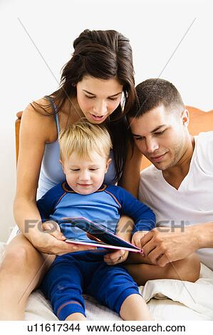 Parents and toddler son reading book in bed View Large Photo Image Picture - Parents and toddler son reading book in bed. Fotosearch