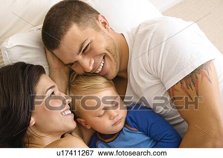 Parents cuddling with toddler son sleeping in bed View Large Photo Image Stock Photo - Parents cuddling with toddler son sleeping in bed. Fotosearch