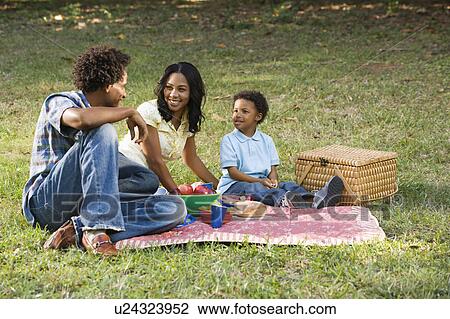 Stock Image - Smiling happy parents and son having picnic in park.. Fotosearch