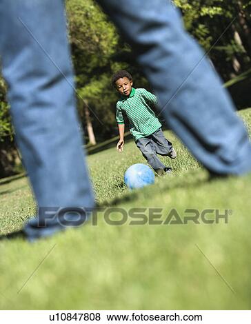 Son running and kicking ball towards father in park. View Large Photo Image Stock Photo - Son running and kicking ball towards father in park.. Fotosearch