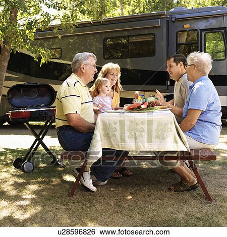 Stock Photograph - Three generation Caucasian family seated at picnic table in front of recreational vehicle talking.. Fotosearch