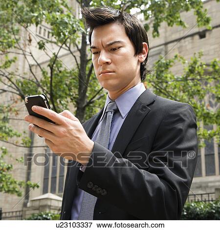 Asian business man standing looking at cell phone messages. View Large Photo Image Stock Photo - Asian business man standing looking at cell phone messages.. Fotosearch