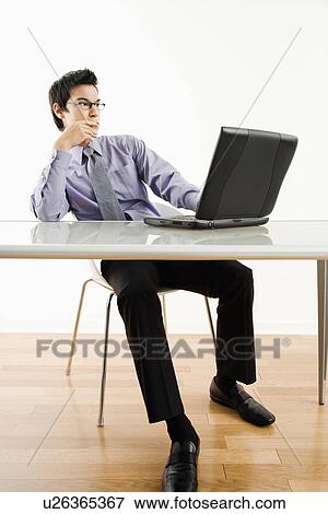 Stock Photo - Asian businessman sitting at desk working on laptop computer.. Fotosearch