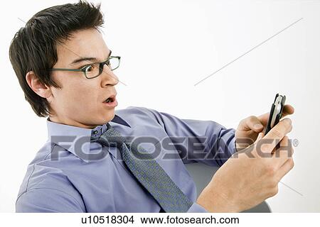 Picture - Asian businessman with surprised expression looking at message on his pda cellphone.. Fotosearch