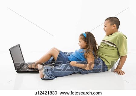 Stock Image - Brother and sister putting feet on laptop computer and smiling.. Fotosearch