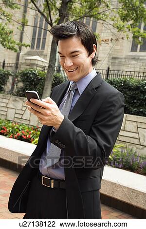 Business man standing looking at cell phone messages smiling View Large Photo Image Stock Image - Business man standing looking at cell phone messages smiling. Fotosearch