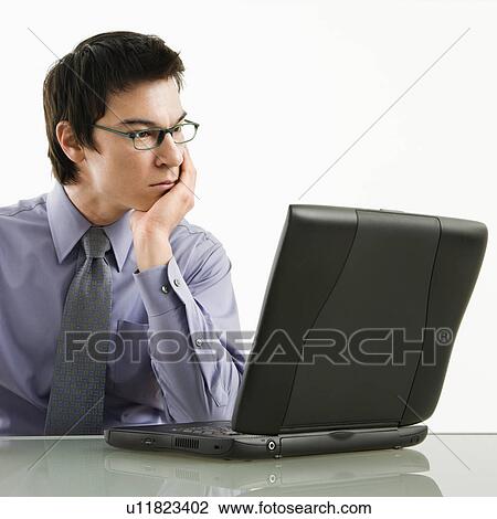 Stock Image - Businessman sitting at desk working on laptop computer. Fotosearch