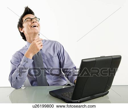 Stock Image - Businessman sitting at desk working on laptop computer laughing. Fotosearch