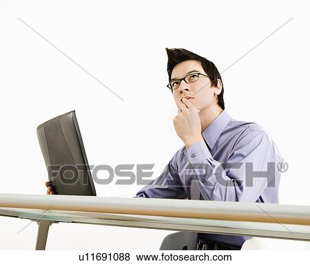 Stock Photo - Businessman sitting at desk working on laptop thinking. Fotosearch