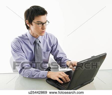 Stock Photo - Businessman sitting at desk working on laptop computer. Fotosearch