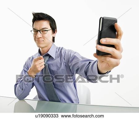 Stock Image - Businessman taking photograph of himself using pda or mobile phone device. Fotosearch