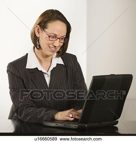 Caucasian businesswoman sitting at desk smiling with laptop computer. View Large Photo Image Stock Photo - Caucasian businesswoman sitting at desk smiling with laptop computer.. Fotosearch