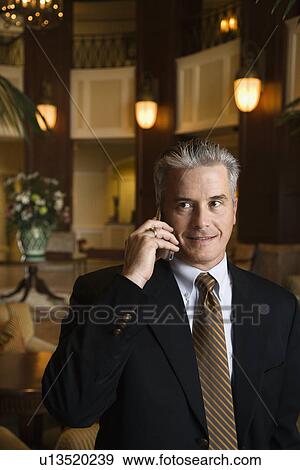 Stock Photo - Caucasian prime adult male businessman talking on cellphone in hotel lobby.. Fotosearch