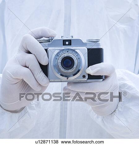 Stock Photo - Man in biohazard suit holding antique camera with finger on shutter button.. Fotosearch