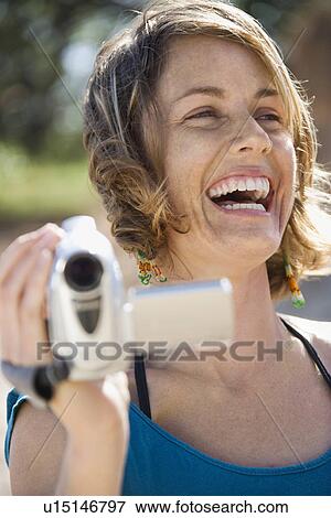 Stock Photo - Mid-adult Caucasian woman outdoors holding video camera laughing.. Fotosearch