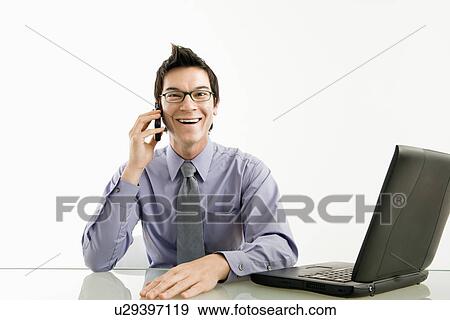Smiling Asian businessman sitting at desk talking on cellphone. View Large Photo Image Stock Photo - Smiling Asian businessman sitting at desk talking on cellphone.. Fotosearch