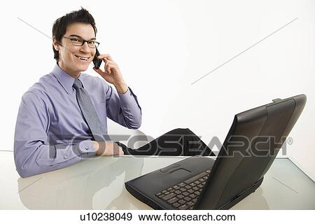Smiling businessman sitting at desk talking on cellphone View Large Photo Image Stock Photo - Smiling businessman sitting at desk talking on cellphone. Fotosearch
