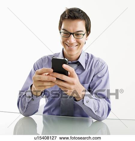 Stock Photo - Smiling businessman sitting at desk texting using his pda cellphone. Fotosearch