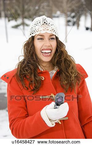 Stock Photo - Young adult female holding cell phone and laughing in snowy climate. Fotosearch