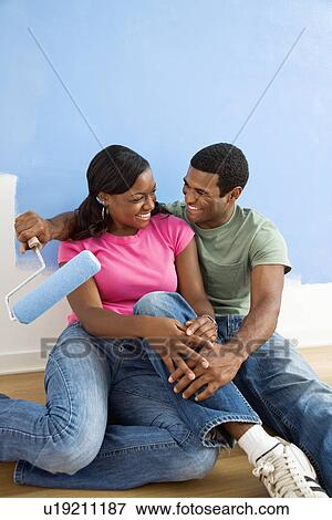 Stock Photo - African American couple relaxing together next to half-painted wall.. Fotosearch