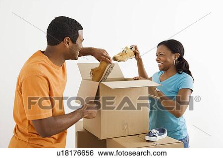 Stock Photograph - African American male and female couple packing cardboard boxes with shoes.. Fotosearch