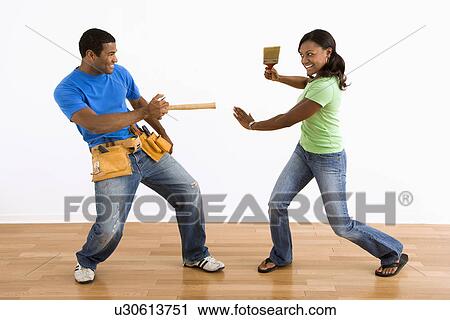 Stock Image - African American man and woman play fighting with household tools.. Fotosearch