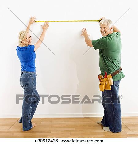 Couple measuring wall with tape measure View Large Photo Image Stock Photograph - Couple measuring wall with tape measure. Fotosearch