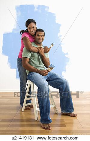 Stock Image - Couple next to half-painted wall. Fotosearch