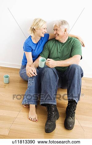 Stock Image - Couple sitting on floor snuggling and drinking coffee. Fotosearch