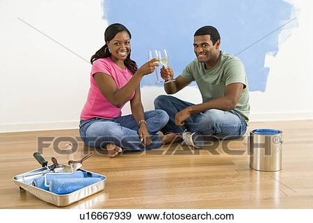 Stock Photo - Couple toasting with wine next to half-painted wall and painting supplies. Fotosearch
