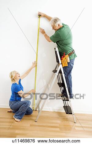 Stock Photograph - Middle-aged couple measuring wall with tape.. Fotosearch