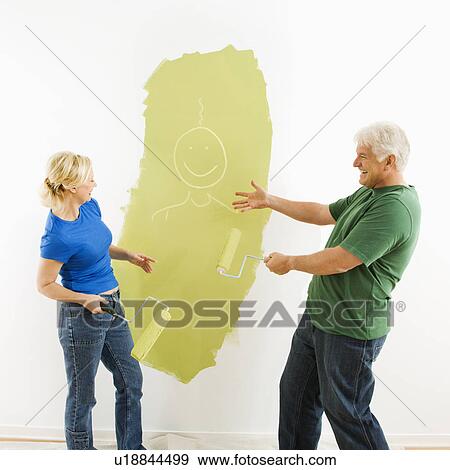 Stock Photo - Middle-aged couple painting wall green finger-painting smiley face figurine for fun.. Fotosearch