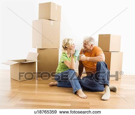 Middle-aged couple sitting on floor among cardboard moving boxes drinking coffee. View Large Photo Image Stock Photo - Middle-aged couple sitting on floor among cardboard moving boxes drinking coffee.. Fotosearch
