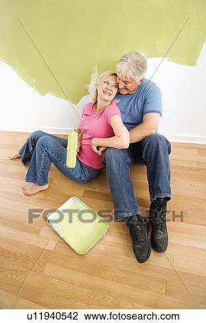 Portrait of happy adult couple sitting in front of half-painted wall with paint supplies snuggling. View Large Photo Image Stock Image - Portrait of happy adult couple sitting in front of half-painted wall with paint supplies snuggling.. Fotosearch