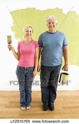 Portrait of happy adult couple standing in front of half-painted wall with paint supplies 'American Gothic' style. View Large Photo Image Stock Photography - Portrait of happy adult couple standing in front of half-painted wall with paint supplies 'American Gothic' style.. Fotosearch