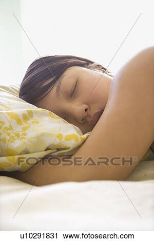 Stock Image - Portrait of pretty young Asian woman lying in bed with head on pillow with eyes closed.. Fotosearch
