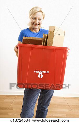 Picture - Portrait of smiling adult blonde woman holding recycling bin full of cardboard. Fotosearch