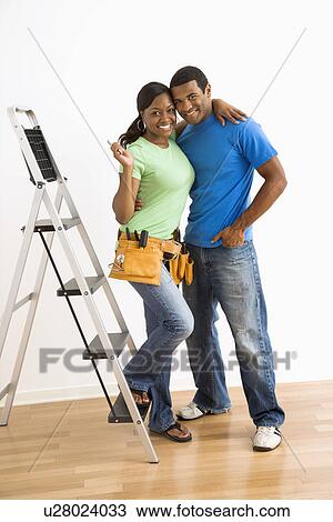 Stock Image - Portrait of smiling African American male and female couple with home repair tools and ladder.. Fotosearch