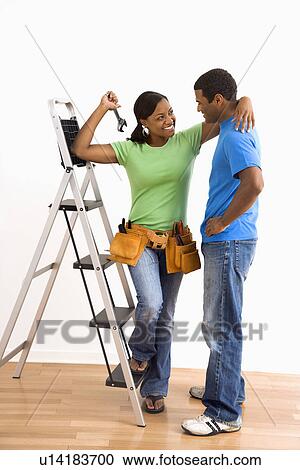 Stock Image - Portrait of smiling male and female couple with home repair tools and ladder. Fotosearch