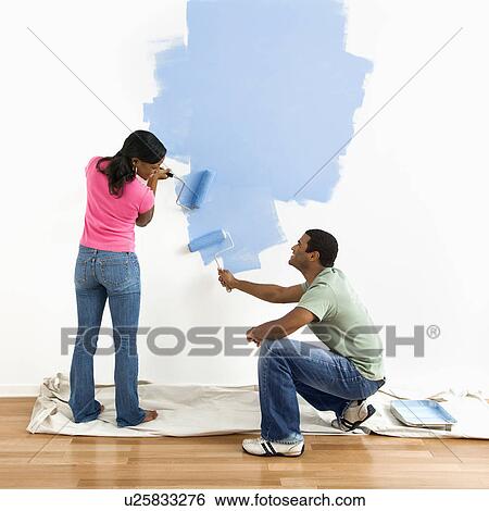 Stock Photograph - Smiling African American male and female couple painting wall blue.. Fotosearch