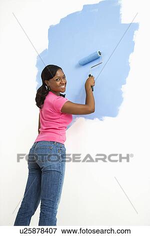 Stock Photo - Woman painting wall blue smiling. Fotosearch