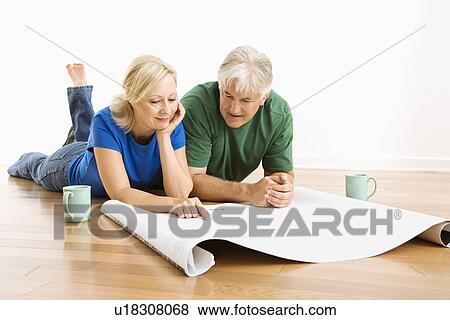 Stock Photo - Couple laying on floor looking at architectural blueprints together. Fotosearch