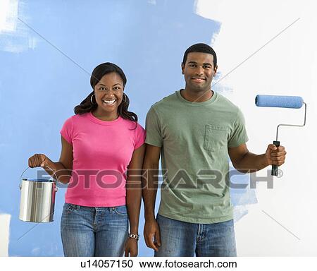 Stock Image - Couple next to half-painted wall with paint supplies. Fotosearch